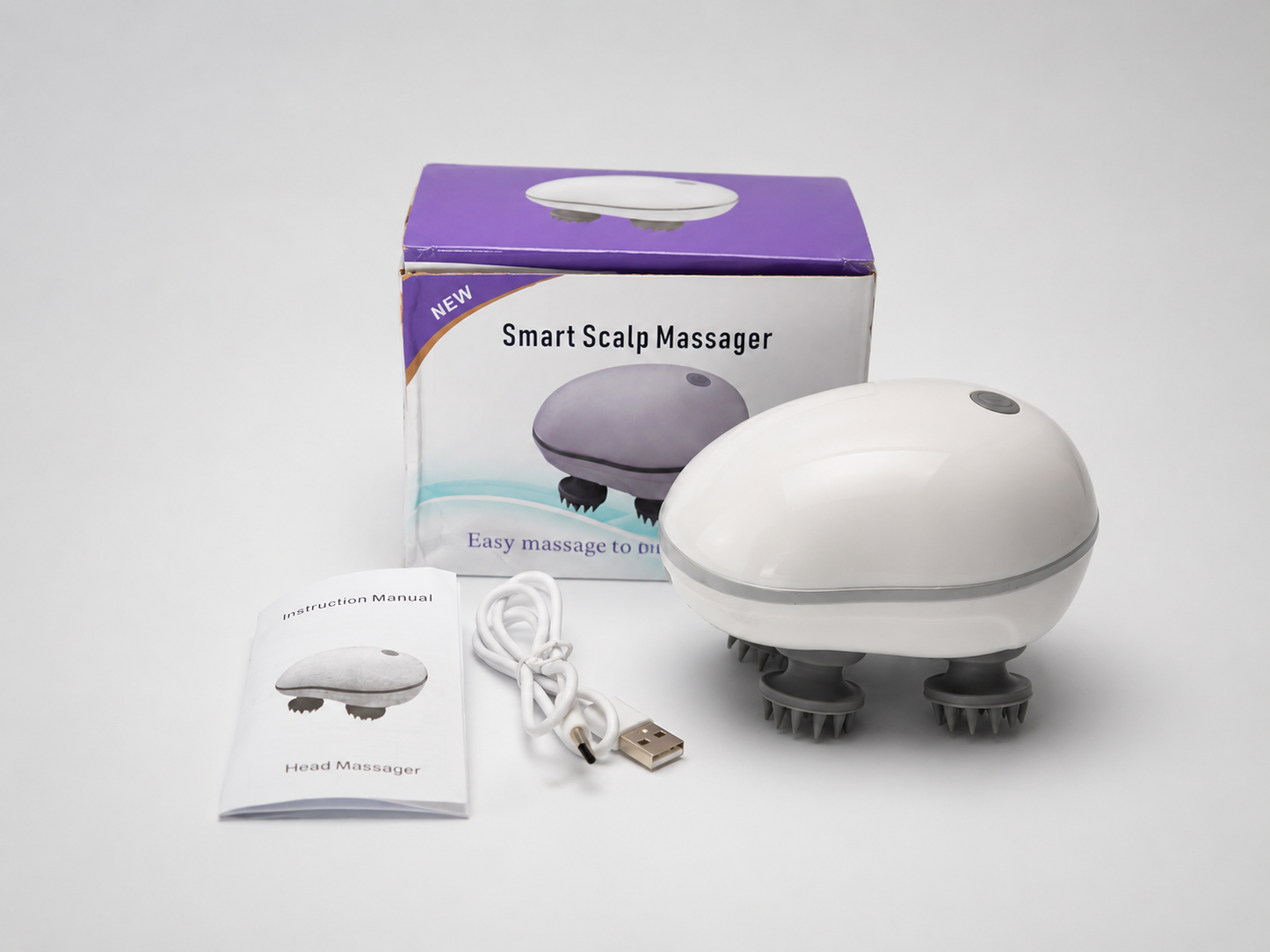A white and gray smart scalp massager shown with its purple and white retail box, a small instruction manual, a white USB charging cable, and a USB connector on a light gray background.